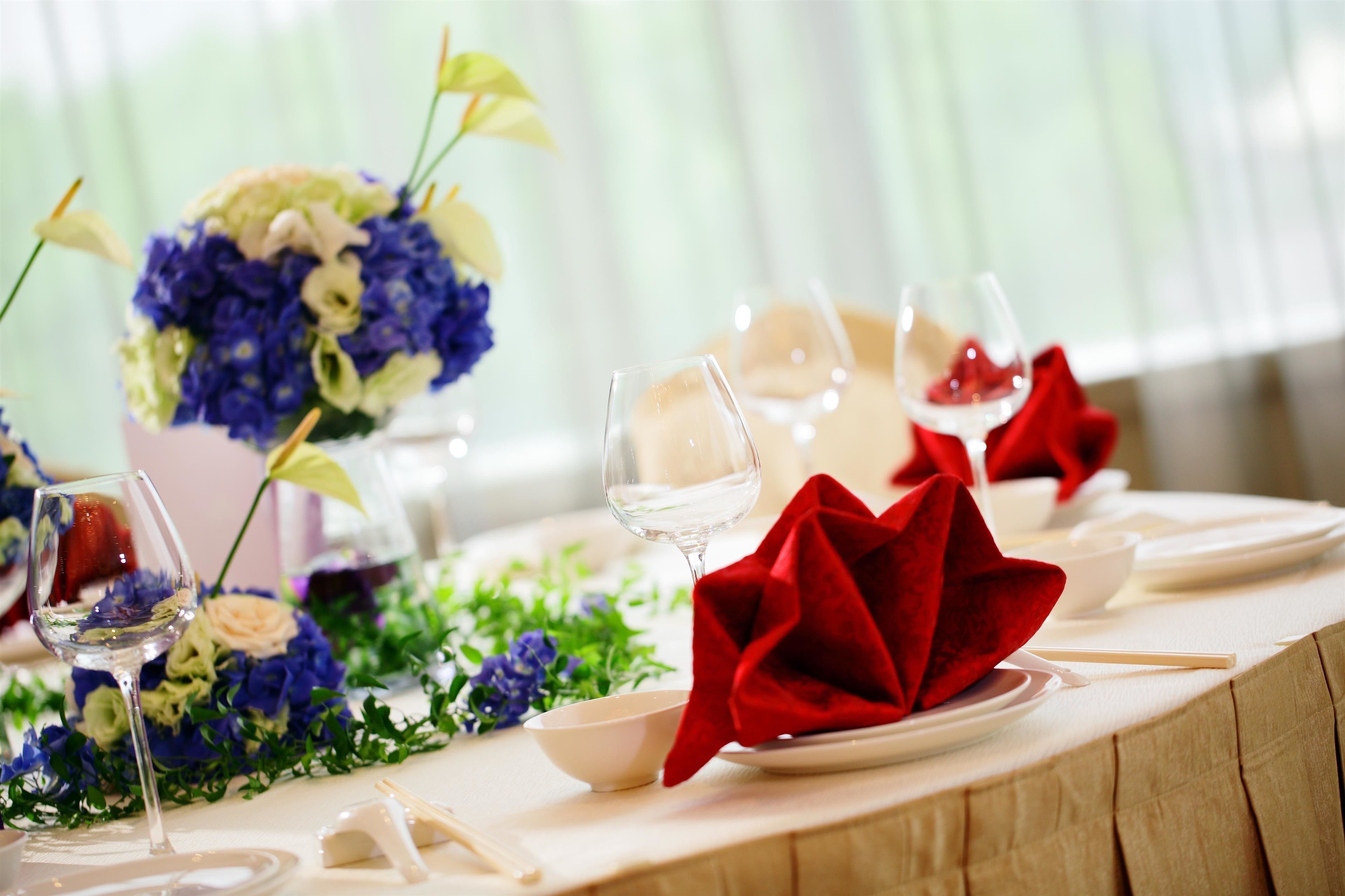 A table set for dining with a vase of flowers, wine glasses, and red napkins.