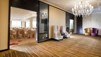 Une pièce spacieuse, dotée d’un grand lustre, d’un coin salon avec des fauteuils et offrant une vue sur une salle de banquet.