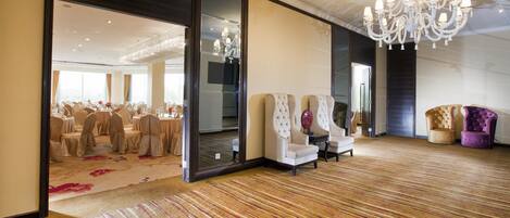 Une pièce spacieuse, dotée d’un grand lustre, d’un coin salon avec des fauteuils et offrant une vue sur une salle de banquet.