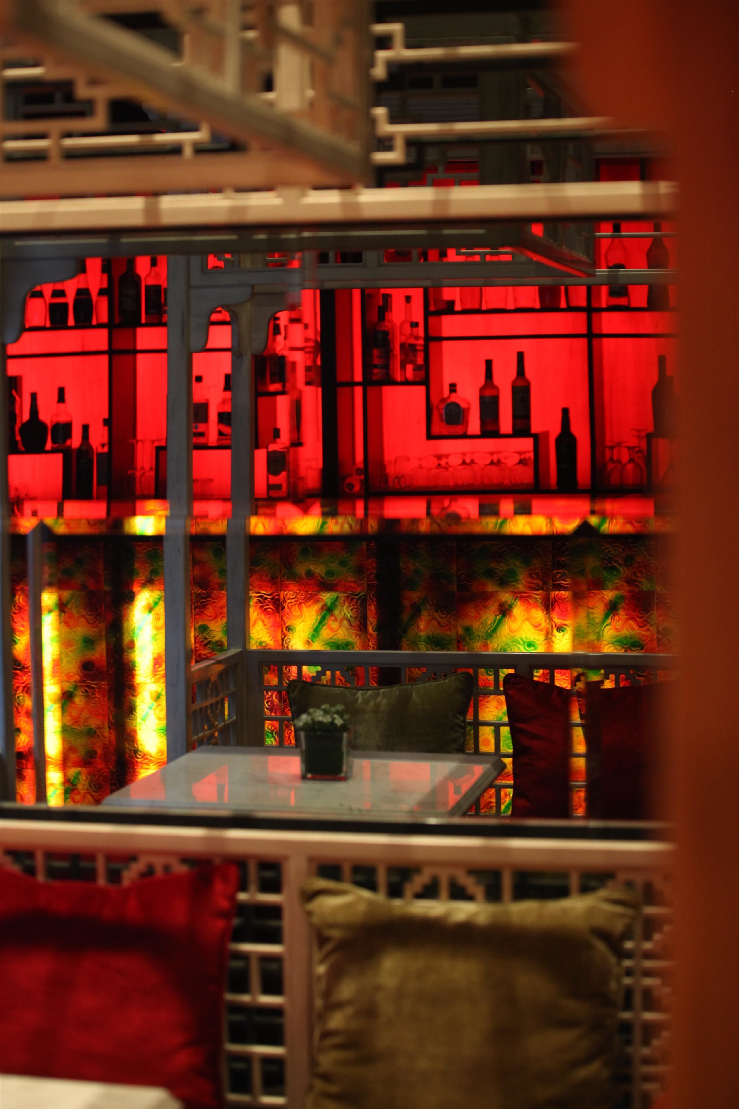 Zona de bar con un fondo iluminado en rojo, una mesa de vidrio y sillas.