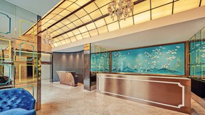 A lobby with a reception desk, a blue sofa, and a large wall mural. - Dorsett Shanghai (Shanghai)