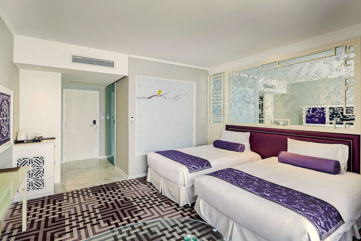 Habitación de hotel con dos camas, un espejo grande, una obra de arte en la pared y una alfombra estampada.