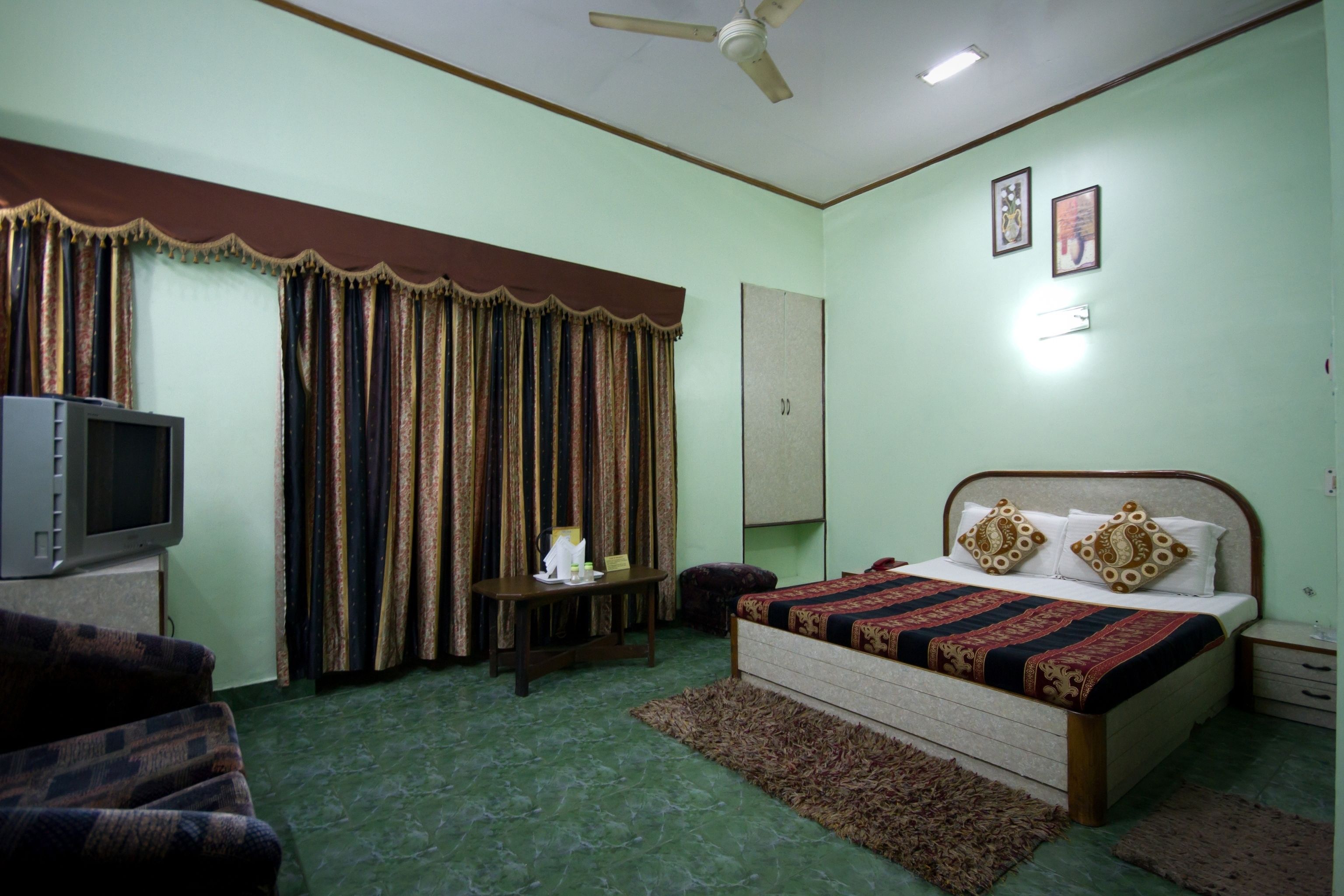A bedroom with a bed, a television, curtains, a desk, and a ceiling fan.