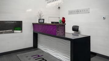A reception area with a modern black reception desk, a small plant, a red vase, and a chandelier.