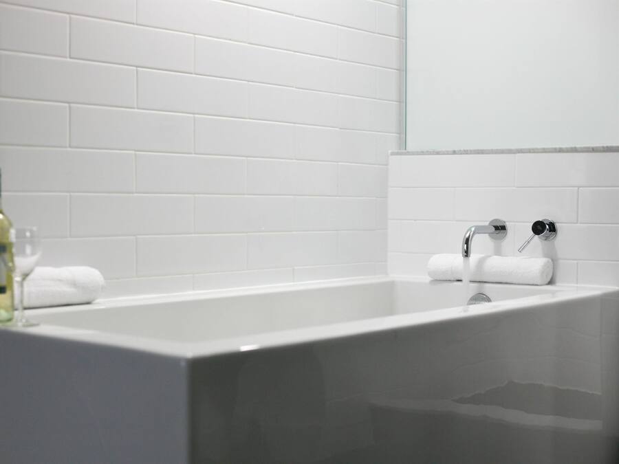 A modern bathroom with a white bathtub, two towel racks, and a bottle of lotion on the side.