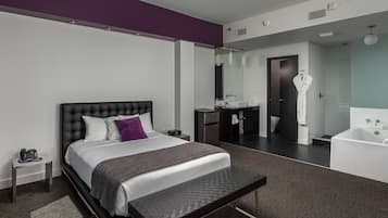 A modern hotel room with a large bed, a bench, a bathroom with a bathtub, and a walk-in closet.