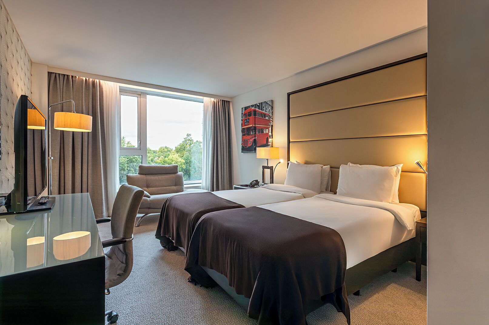 Een hotelkamer met twee bedden, een bureau, een stoel en een groot raam met gordijnen.