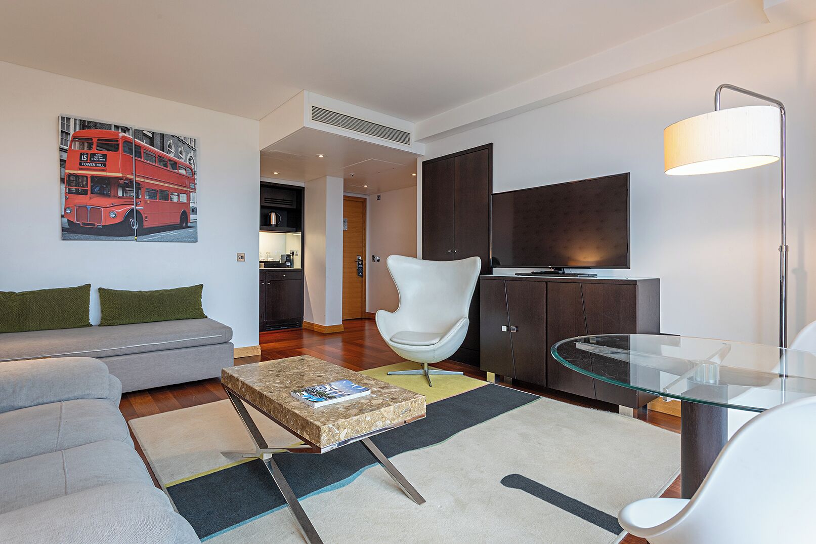Ein modernes Wohnzimmer mit einer Couch, einem Glastisch, einem weißen Sessel, einem Fernseher und einer Lampe.