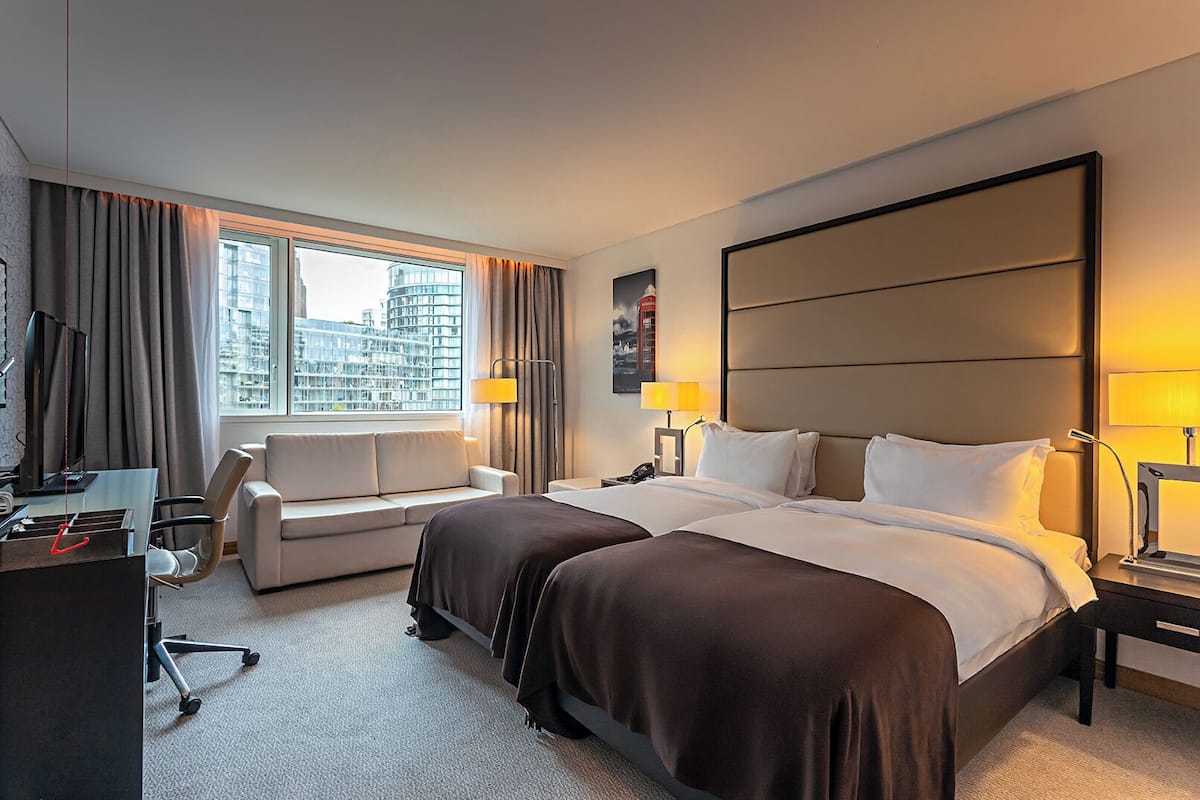 A hotel room with a large bed, a sofa, a desk with a chair, a TV, and a window with curtains.