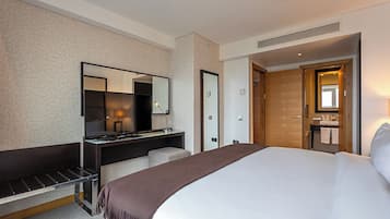 A hotel room with a bed, a desk with a mirror, a chair, and a bathroom visible through an open door.
