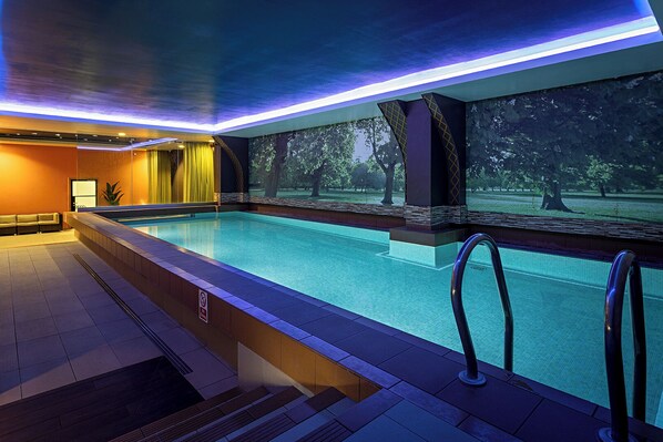 An indoor swimming pool with a view of trees, a sofa, and a staircase. - Pestana Chelsea Bridge Hotel & SPA (London)