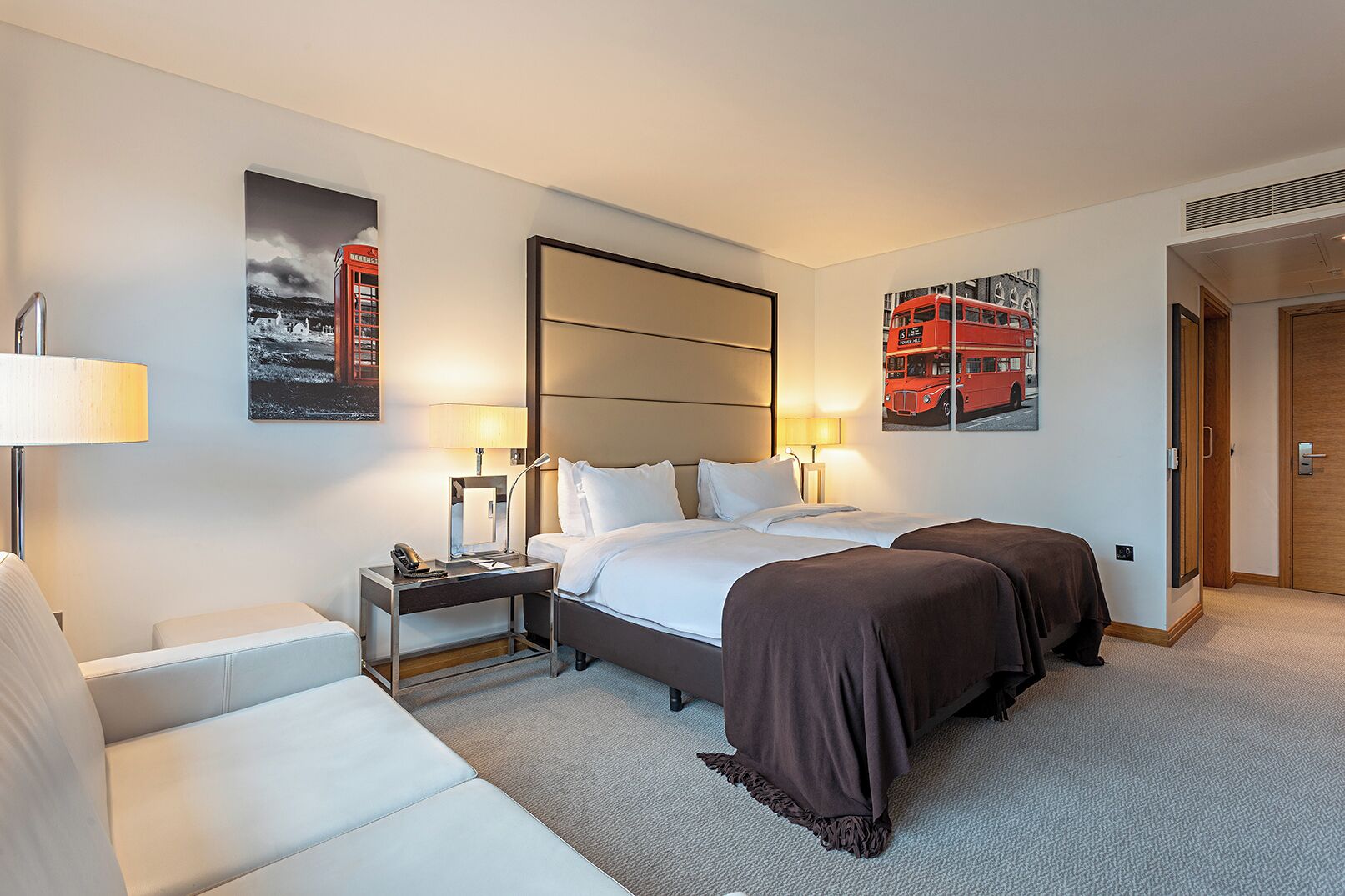 A hotel room with a bed, bedside tables, a lamp, a chair, and two artwork pieces on the walls.