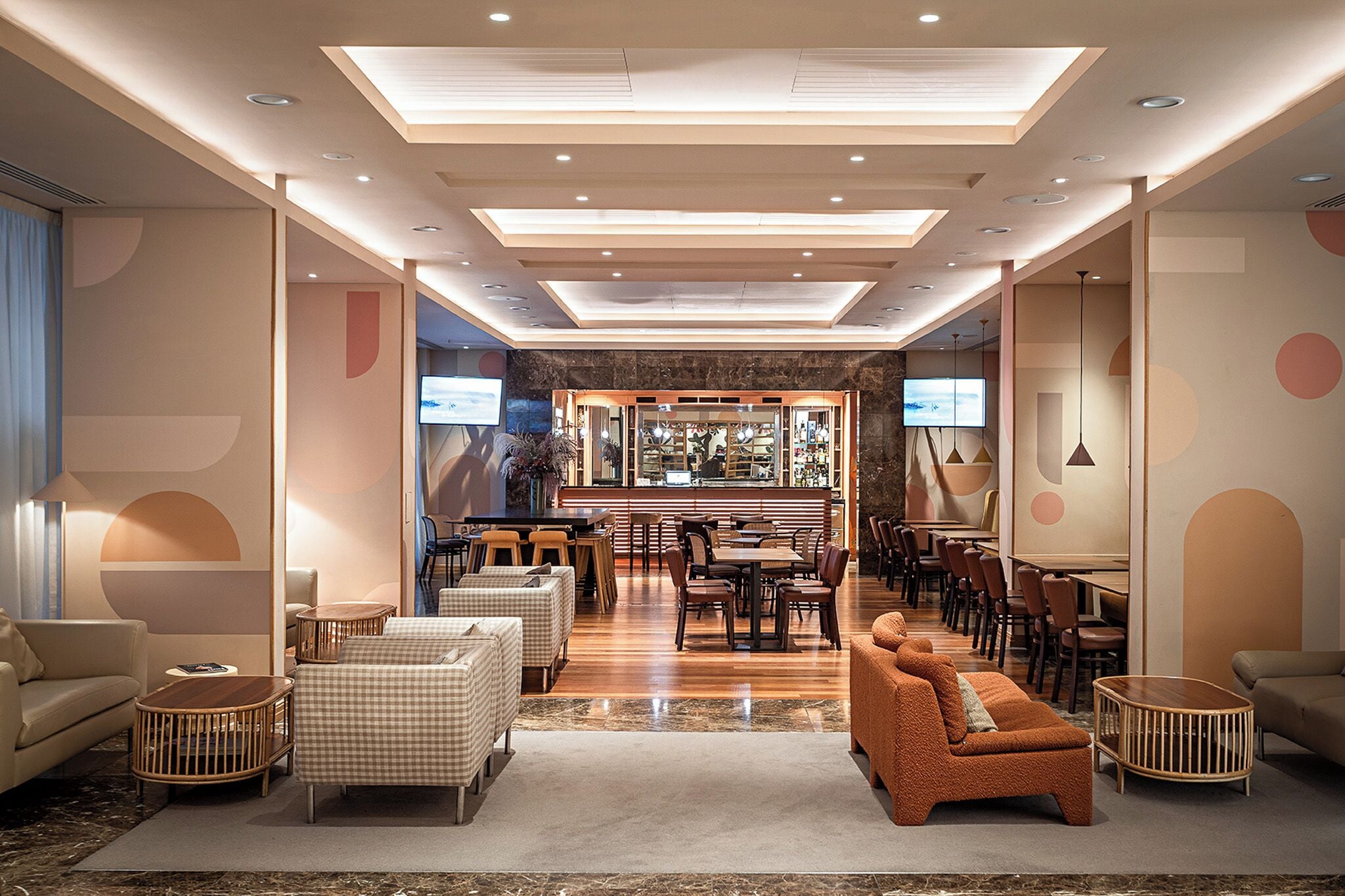 A modern hotel lobby with a bar area, seating arrangements, and a television screen.
