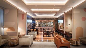 A modern hotel lobby with a bar area, seating arrangements, and a television screen.
