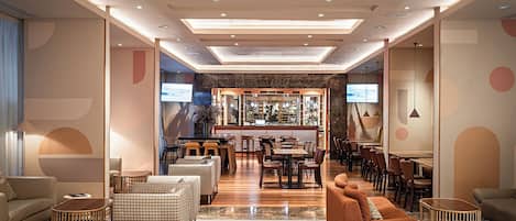 A modern hotel lobby with a bar area, seating arrangements, and a television screen.