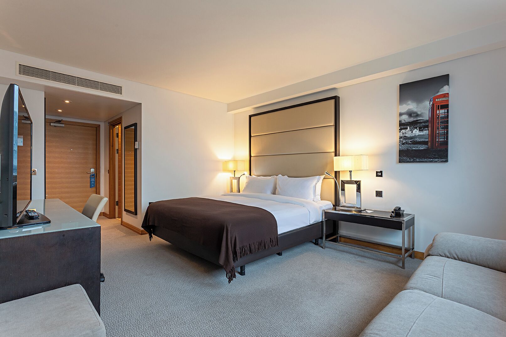 Ein Hotelzimmer mit einem Bett, Nachttischen, einem Schreibtisch, einem Sessel und einer Couch.