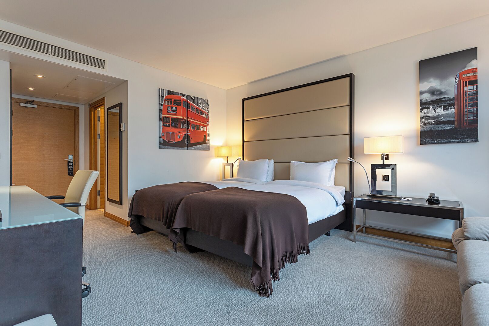 A hotel room with a bed, bedside tables, a desk, and chairs.