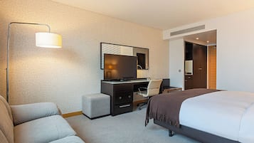 Ein Hotelzimmer mit einem Bett, einem Schreibtisch mit Computer, einem Sessel und einer Couch, sowie einer Lampe.