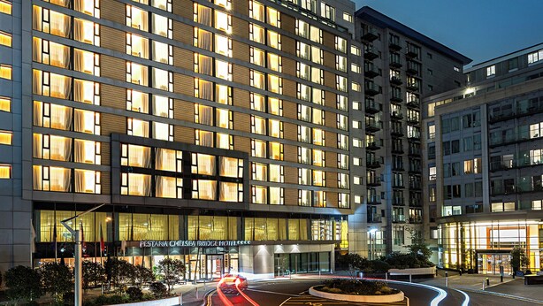 A multi-story hotel with a modern facade, large windows, and a well-lit entrance. - Pestana Chelsea Bridge Hotel & SPA (London)