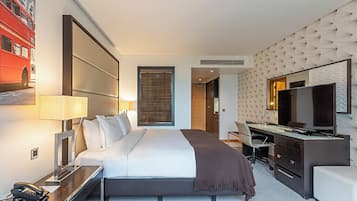 A hotel room with a bed, desk, chair, TV, and a large window with blinds.