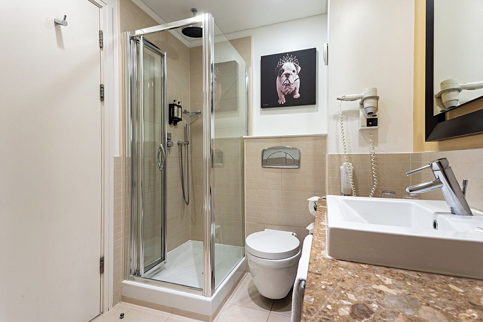 A modern bathroom with a glass-enclosed shower, a white toilet, a sink with a mirror, and a framed picture on the wall.