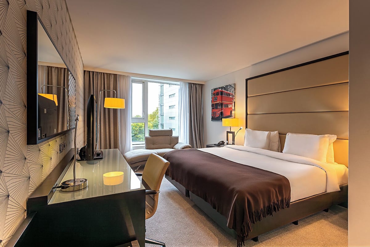 A hotel room with a bed, desk, chair, and a large mirror.