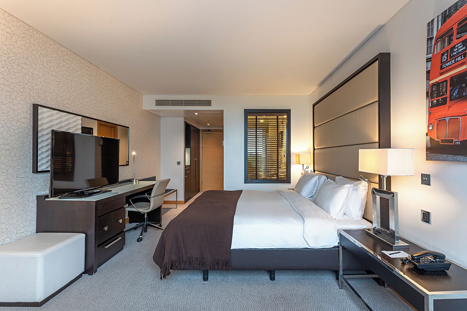 A hotel room with a bed, desk, chair, and a large mirror.