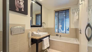 A bathroom with a bathtub, a sink, a mirror, a telephone, and a window with blinds.