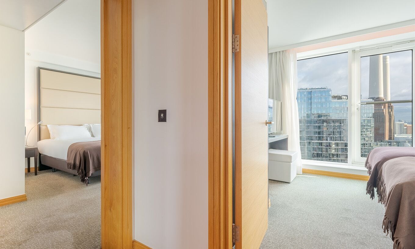 Une chambre d’hôtel avec un lit, un bureau, une chaise, une fenêtre donnant sur la ville et une porte.