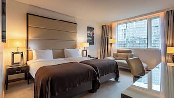 A hotel room with two beds, a sofa, a desk, and a large window with a city view.