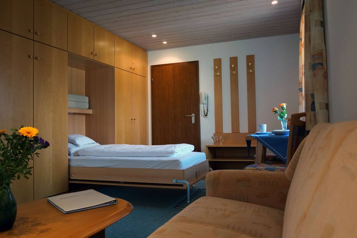 A bedroom with two beds, a desk with a chair, a vase with flowers, and a wooden wardrobe.