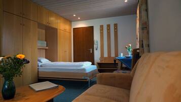 A bedroom with two beds, a desk with a chair, a vase with flowers, and a wooden wardrobe.