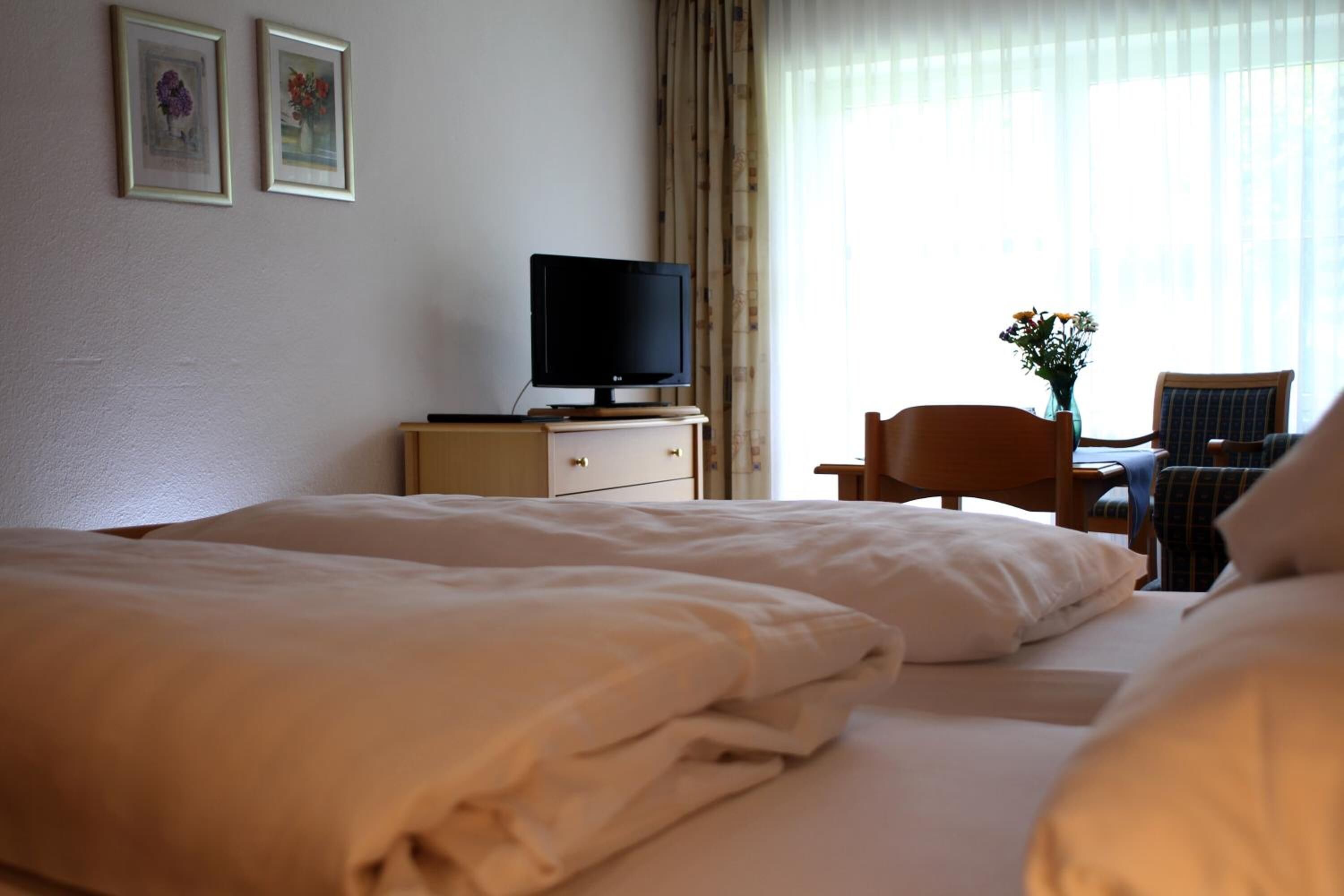 Une chambre d’hôtel avec deux lits, un bureau avec une chaise, une télévision et un vase avec des fleurs.