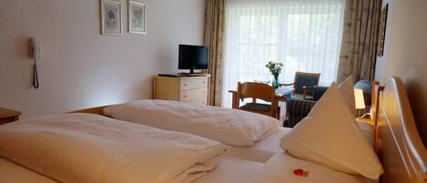 Ein Hotelzimmer mit zwei Betten, einem Schreibtisch mit Stuhl, einem Fernseher und einem Telefon an der Wand.