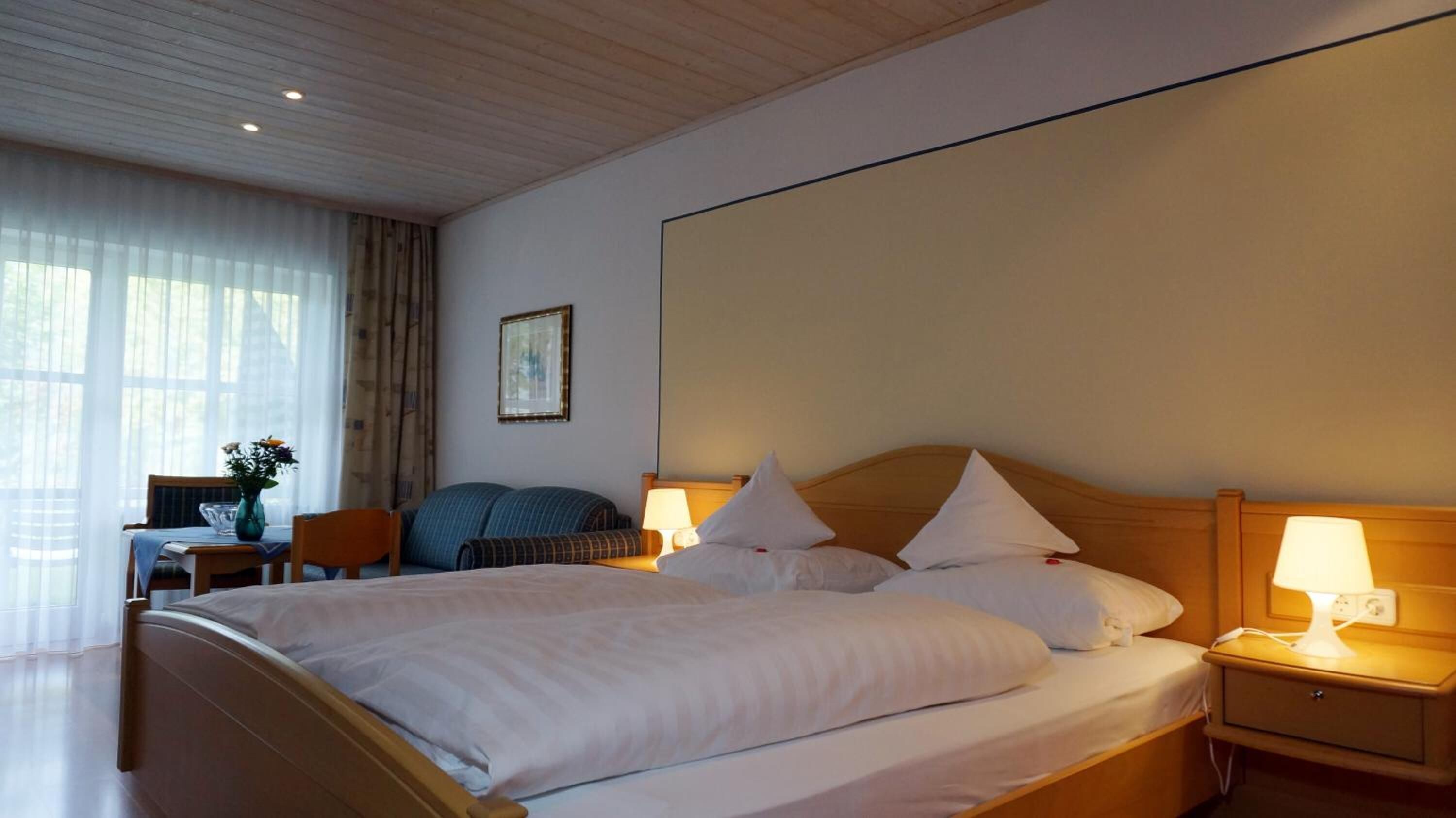 A hotel room with a large bed, bedside lamps, a desk with a chair, and a window with curtains.