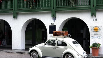 A vintage white car parked in front of a building with green balconies and arched doorways.