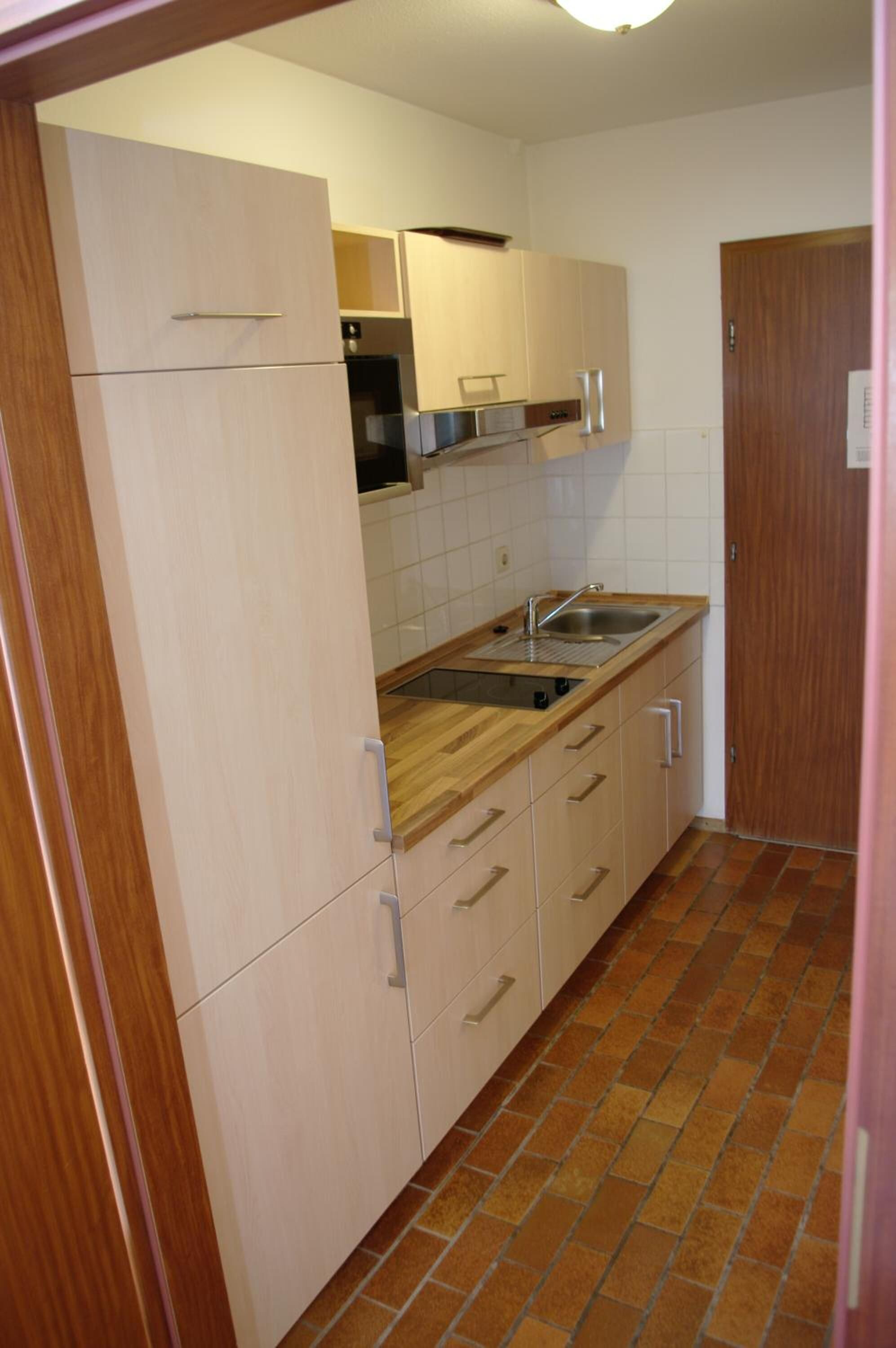 A compact kitchen with light-colored cabinets, a wooden countertop, and a tiled backsplash.