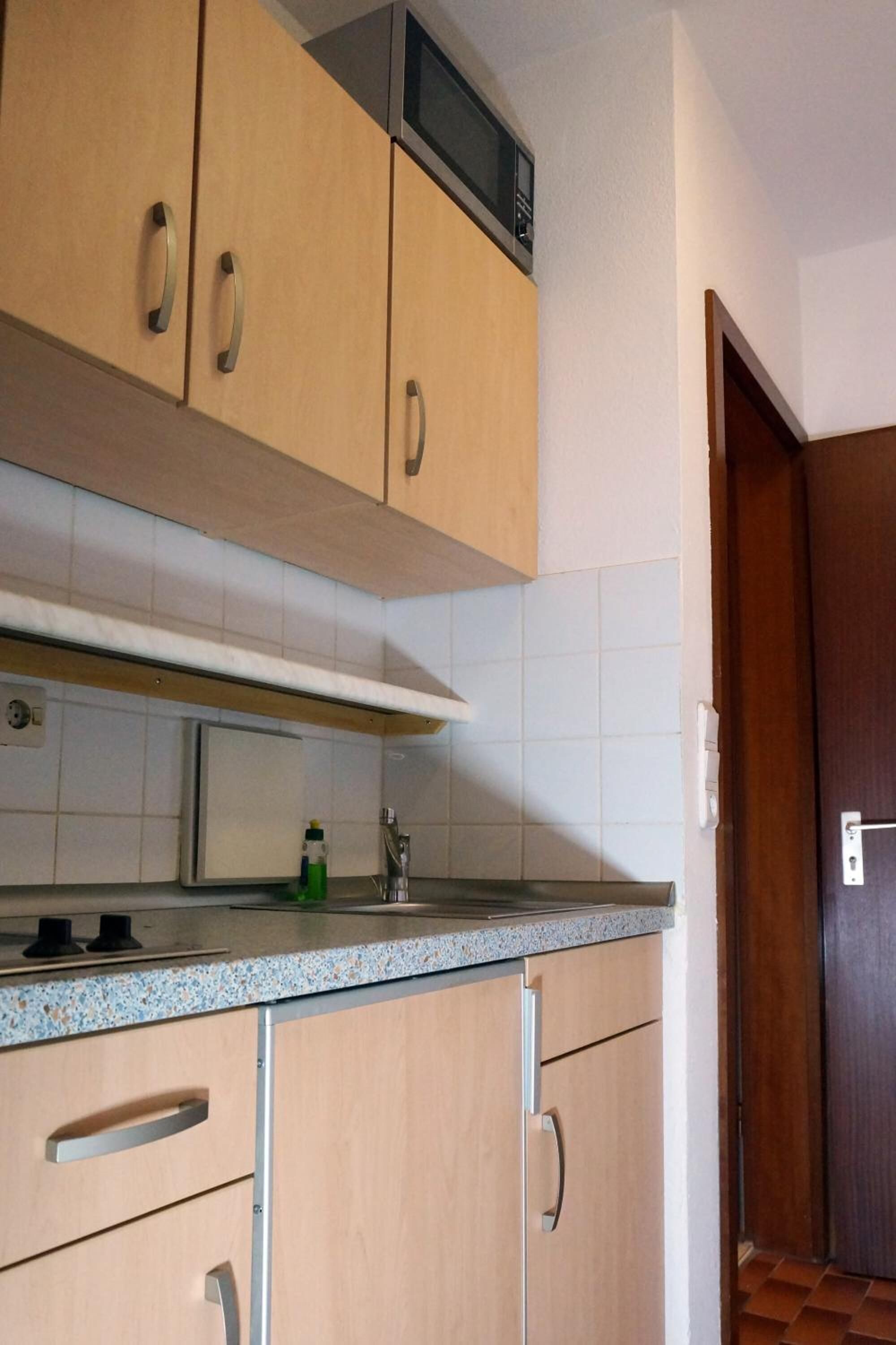 Una cocina con armarios de madera, un microondas y un lavamanos de acero inoxidable.