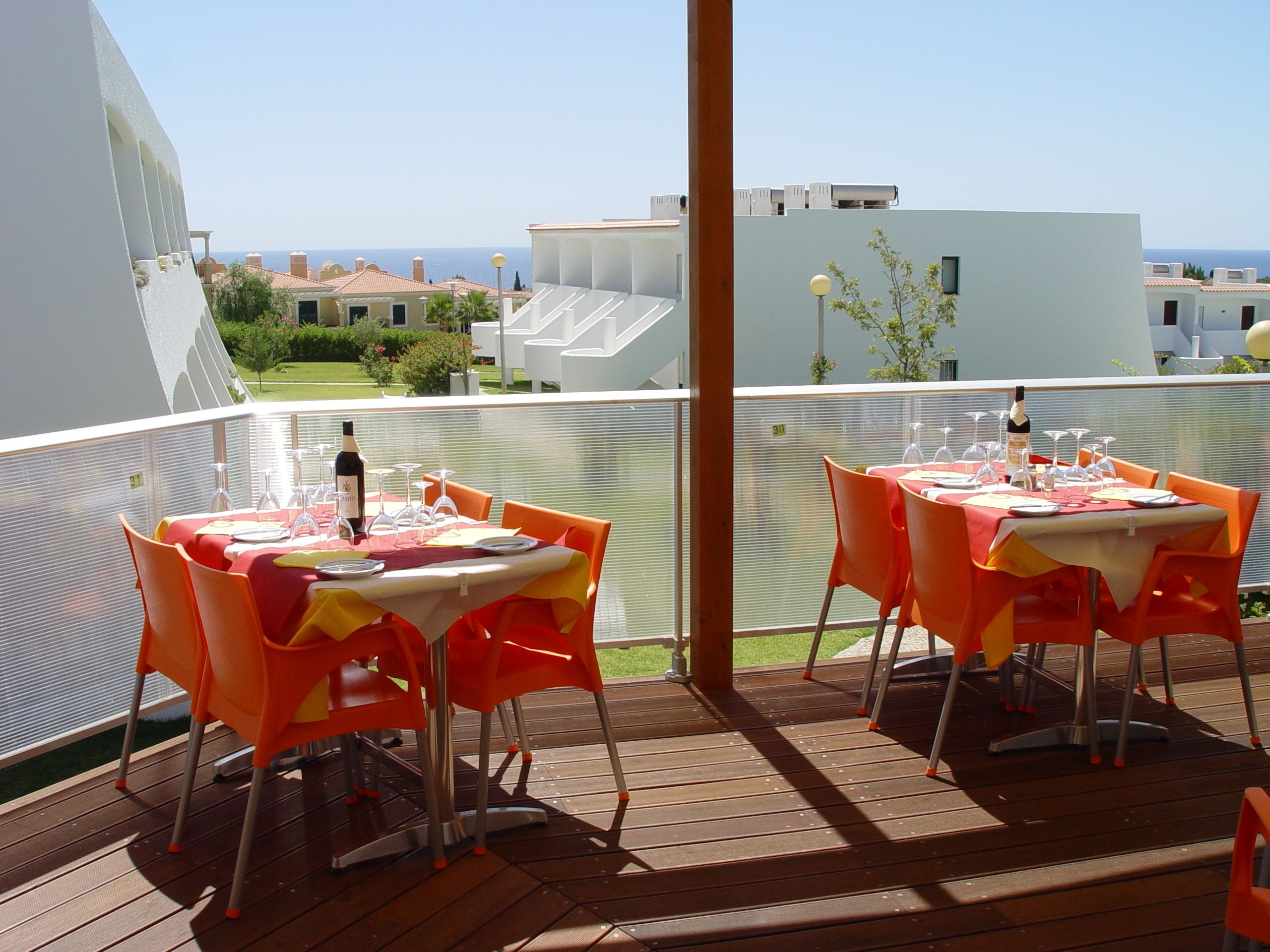A terrace with tables set for dining, overlooking a residential area with buildings and a clear sky.
