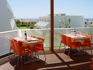 Een terras met gedekte tafels, met uitzicht op een woonwijk met gebouwen en een heldere lucht.