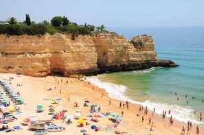 A beach with a rocky cliff, clear blue water, and people sunbathing and swimming. - Quinta das Figueirinhas & Quintinha Village (Lagoa)