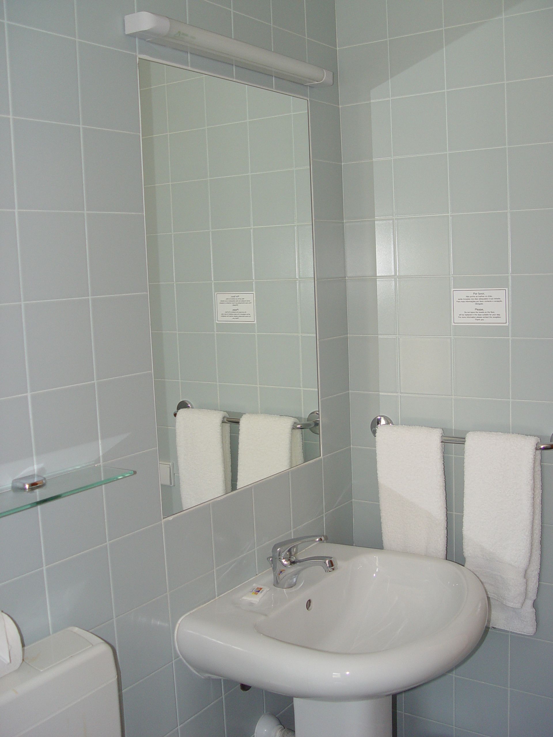 Un baño con un lavabo blanco, un espejo y dos toallas blancas colgadas en un perchero.