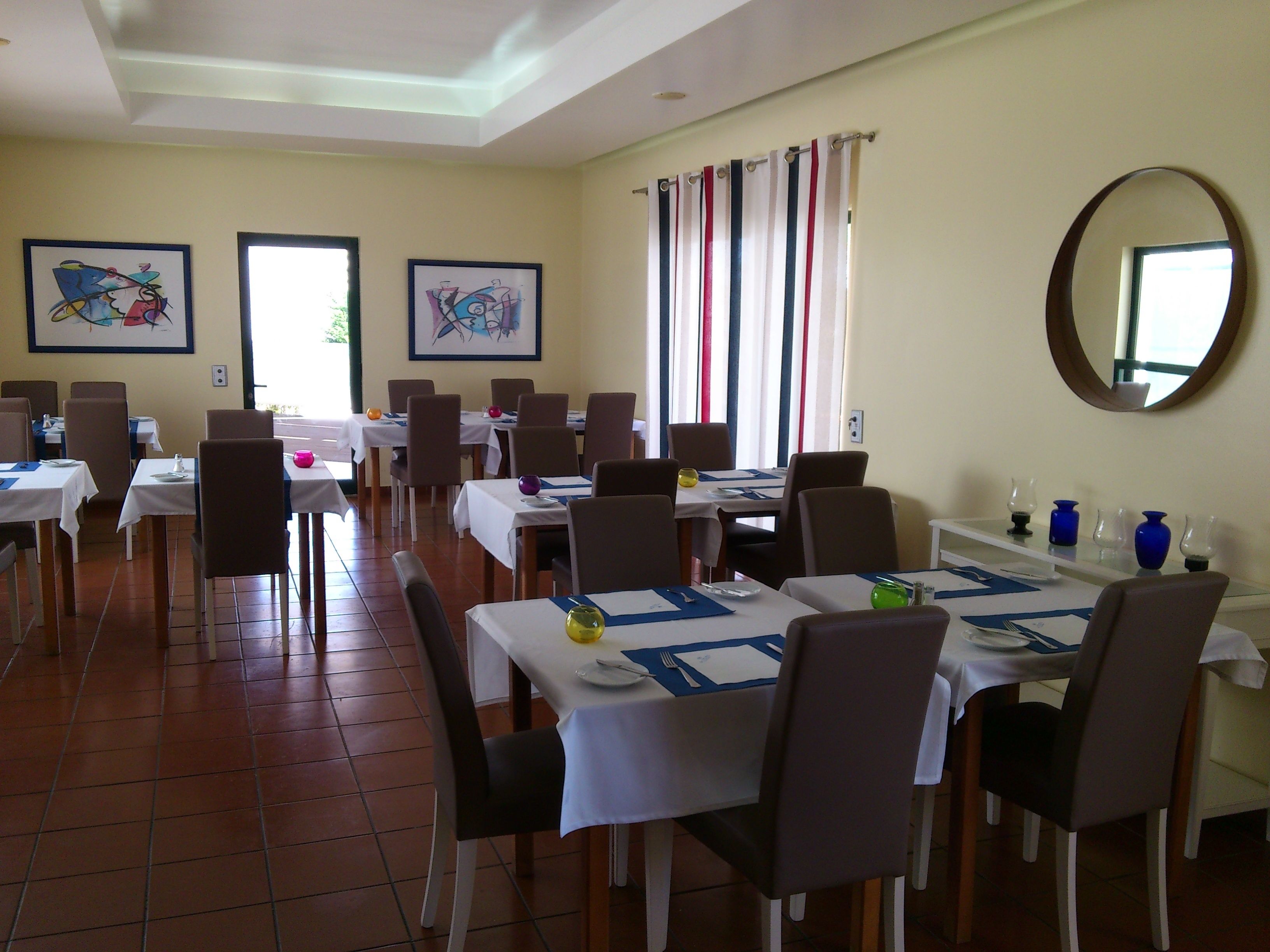 A dining area with multiple tables and chairs, framed artwork on the walls, and a large mirror.
