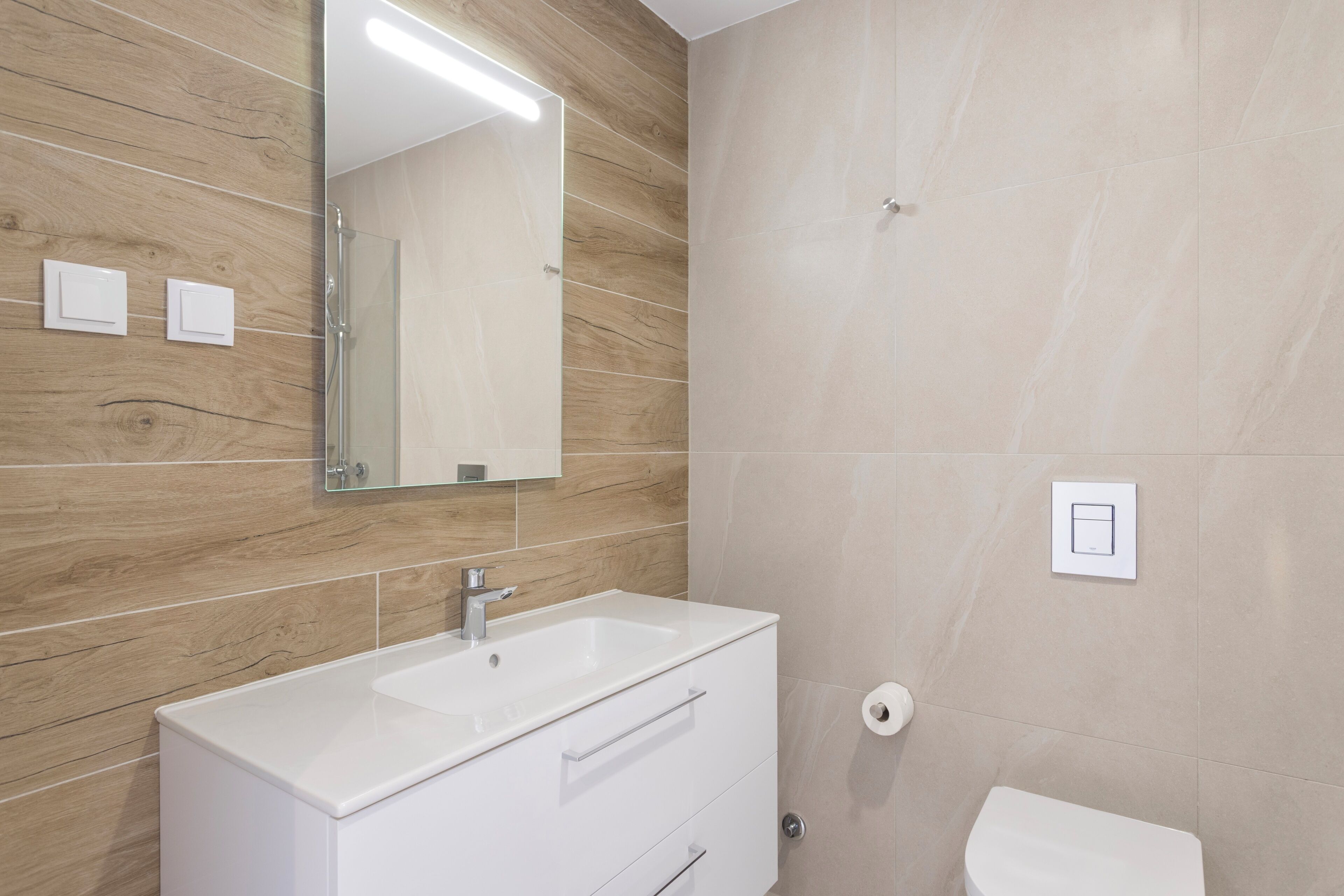 Een badkamer met een wit badkamermeubel, een spiegel, een douche en een toilet.