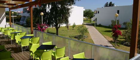 Un espacio de estar al aire libre cubierto con sillas y mesas verdes, con vistas a un césped cuidado y edificios blancos.