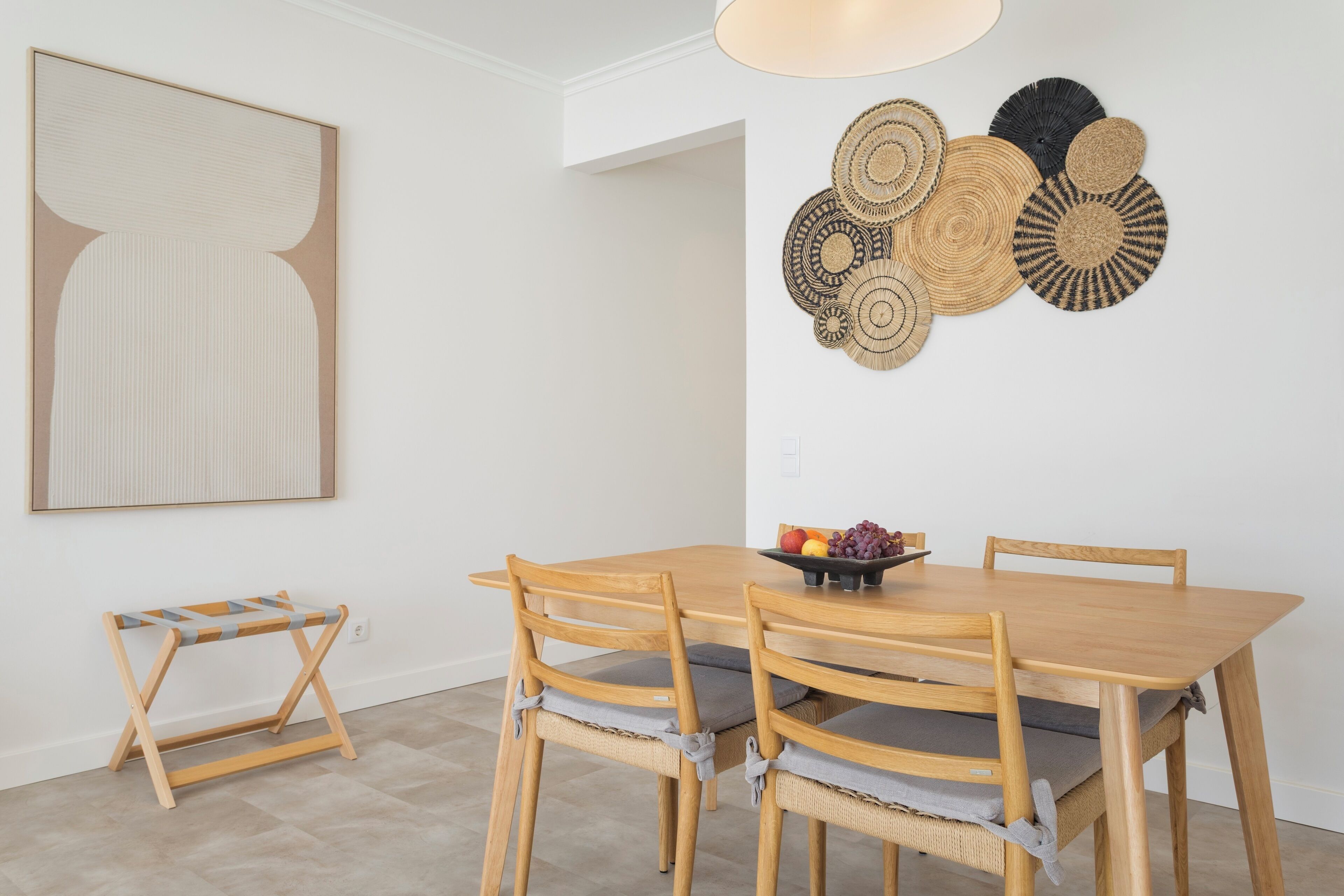 A dining area with a wooden table and chairs, a wall-mounted fruit bowl, and a large abstract painting.