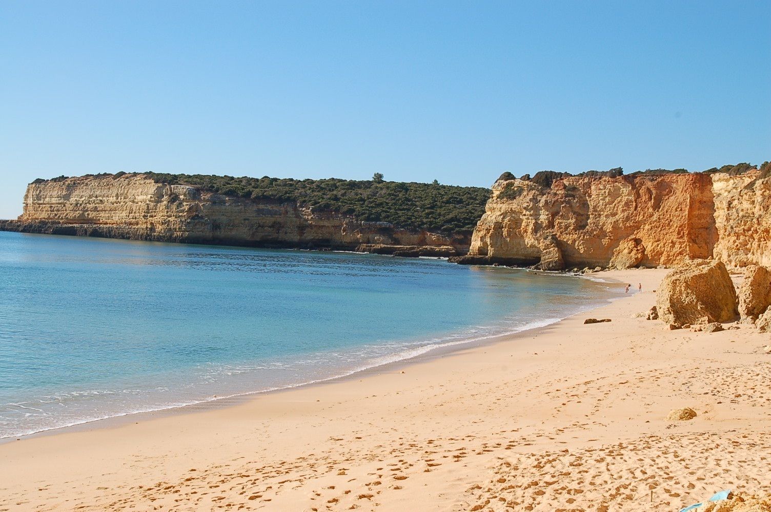A beach with clear blue water, sandy shore, and rocky cliffs.