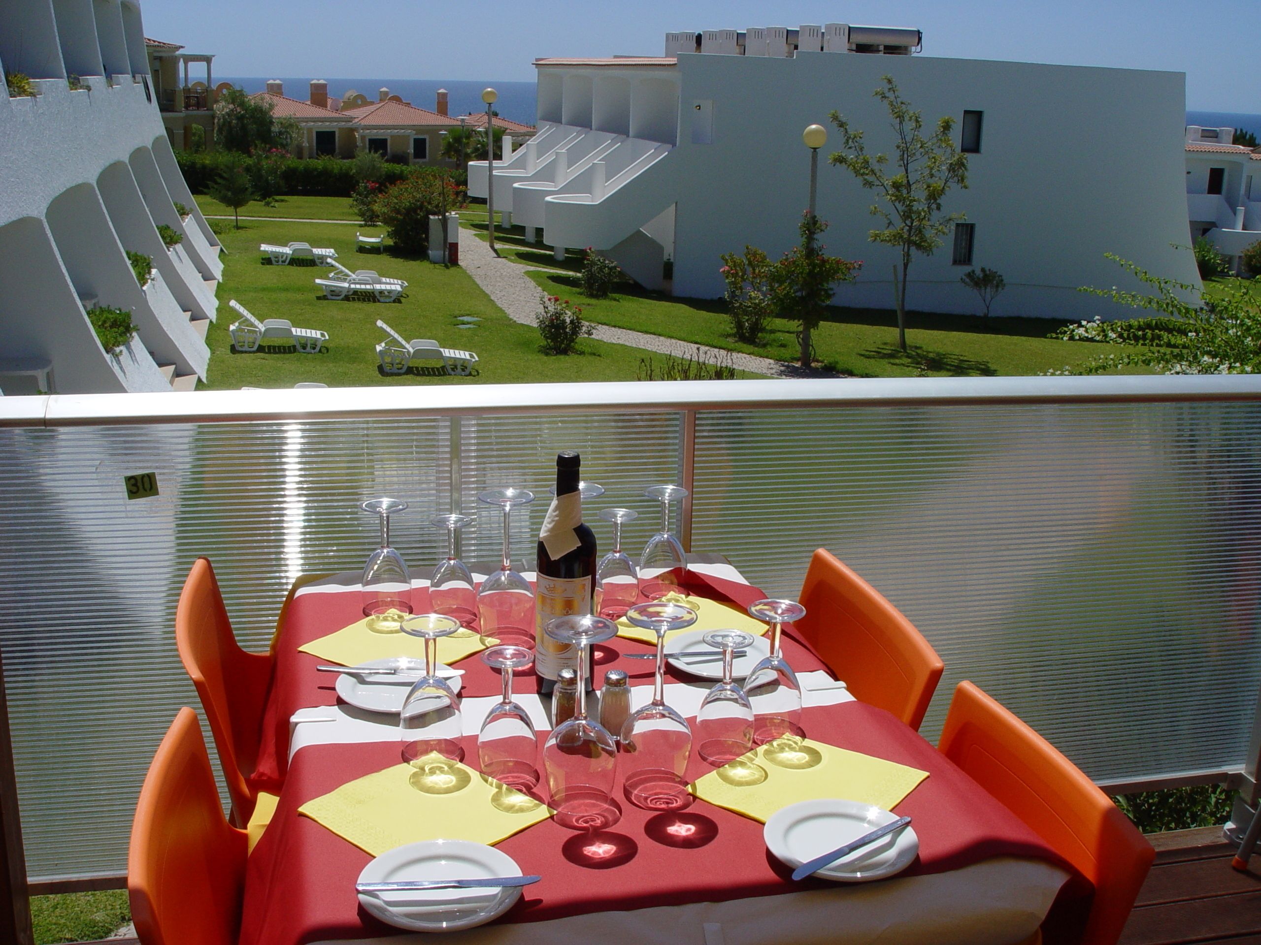A balcony with a table set for six, overlooking a pool and buildings.