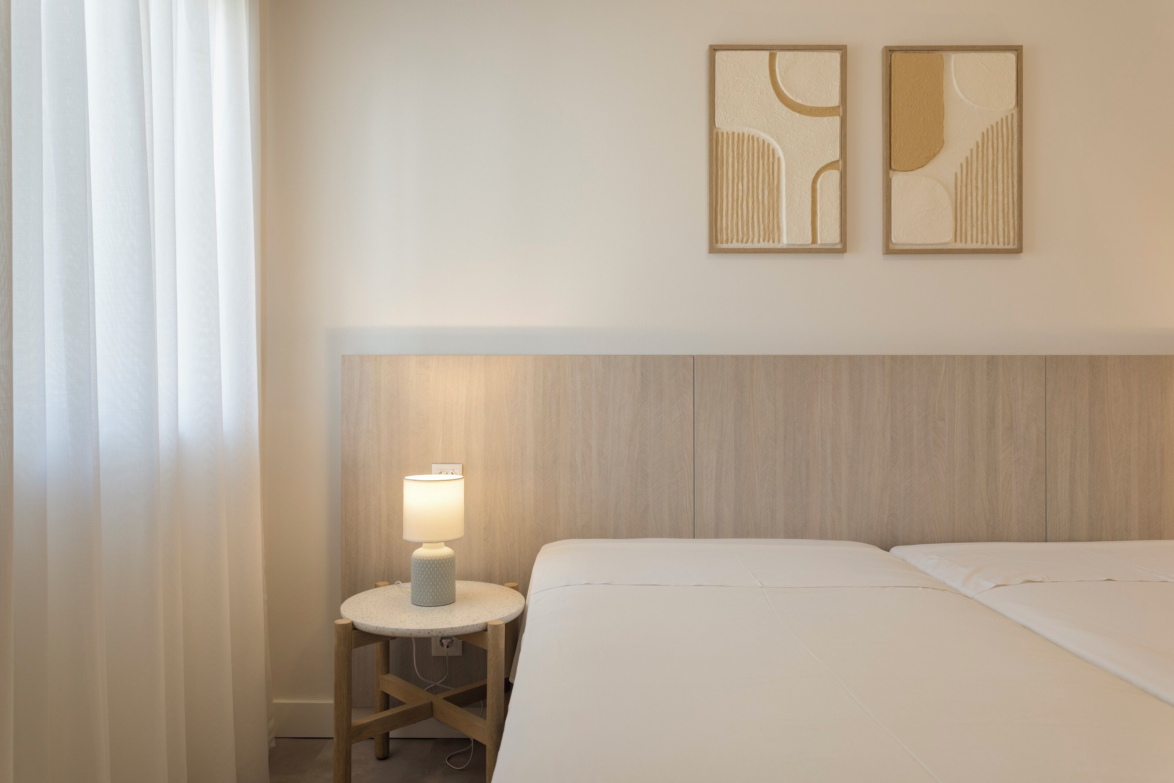 A hotel room with a bed, a nightstand with a lamp, and two wall art pieces.
