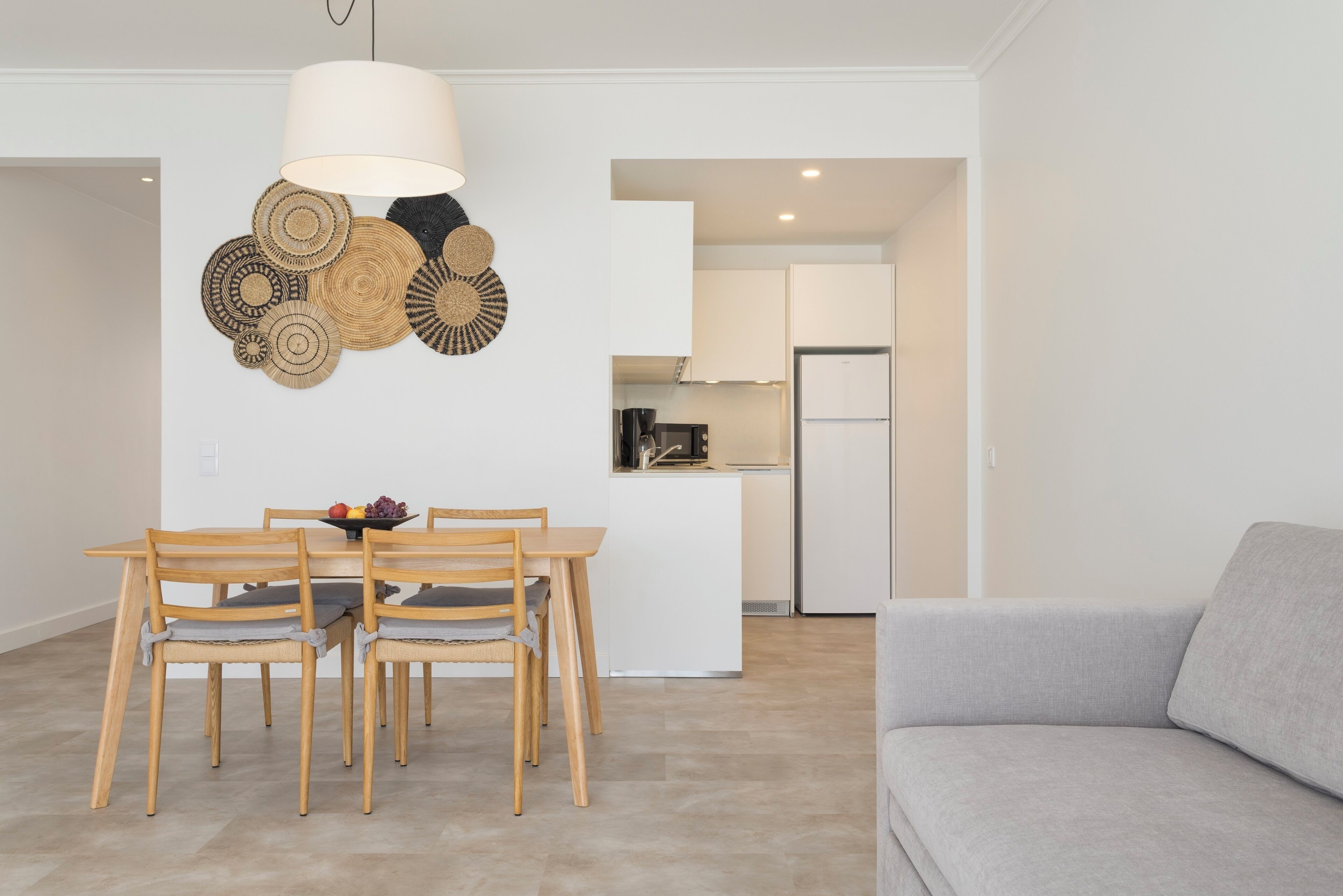 A modern living space with a dining area, kitchenette, and a grey sofa.